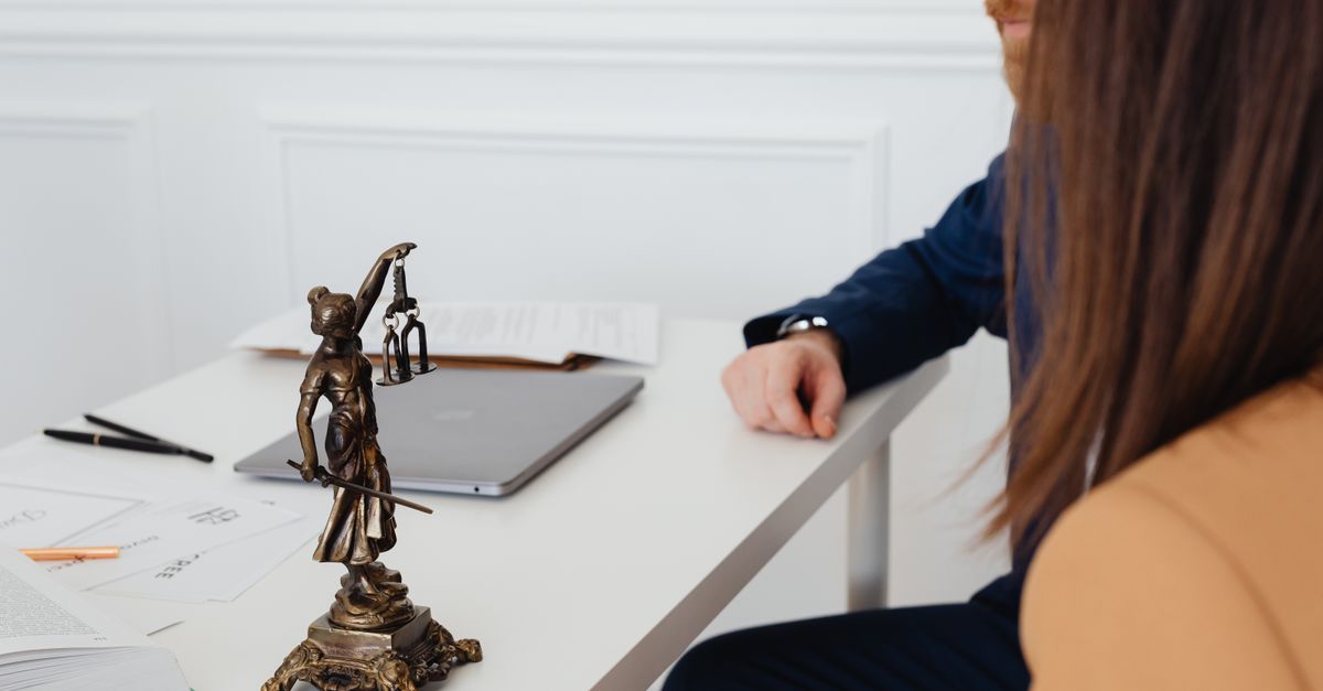 Professional setting with lawyers and Lady Justice statue discussing legal documents.